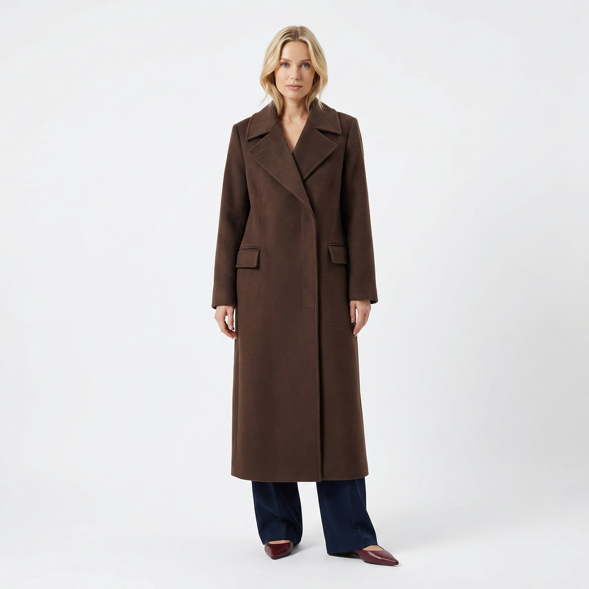 Blonde woman in long brown wool overcoat with wide lapels, front pockets, dark pants, and heels