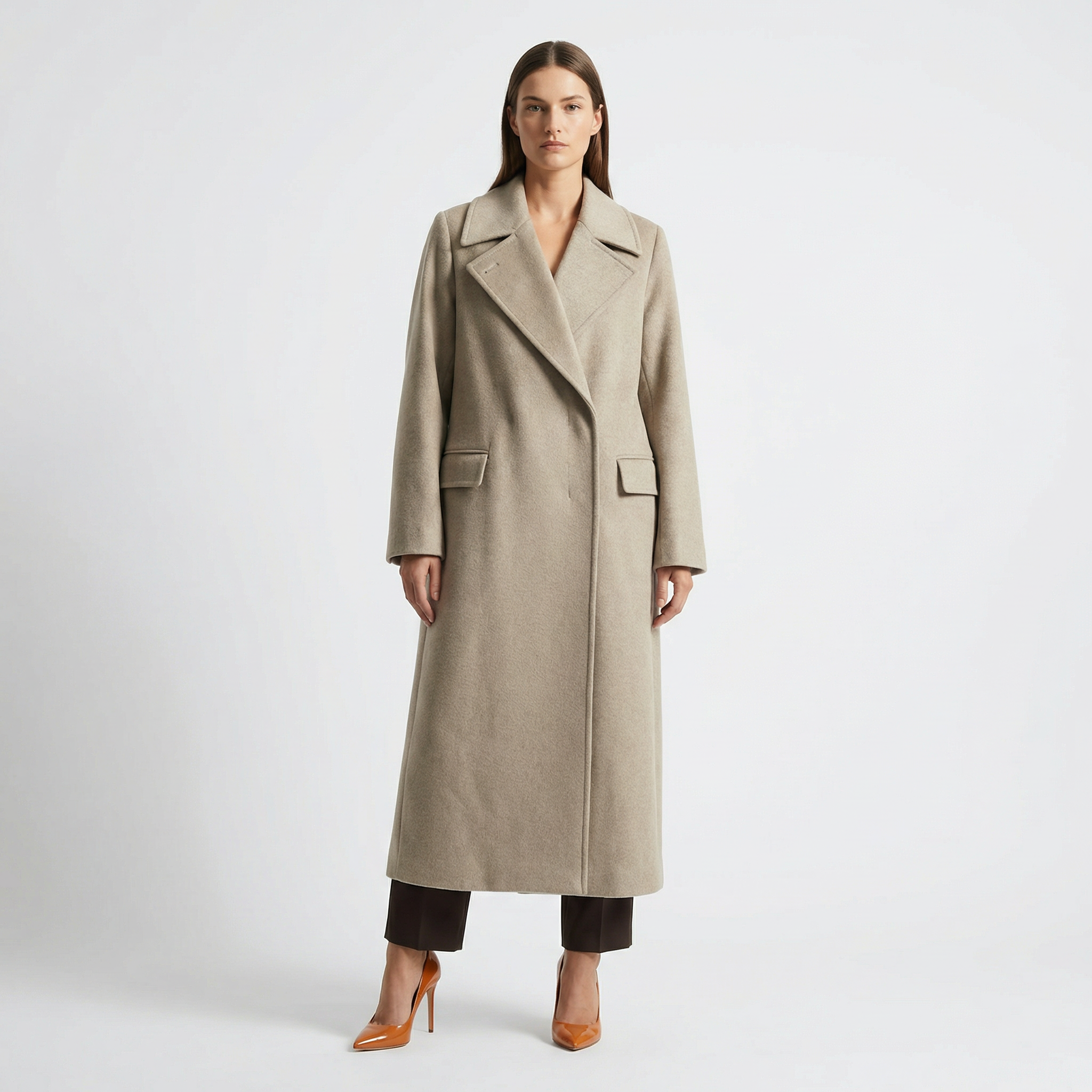 Woman modeling a long beige wool coat with wide lapels, brown pants, and tan heels