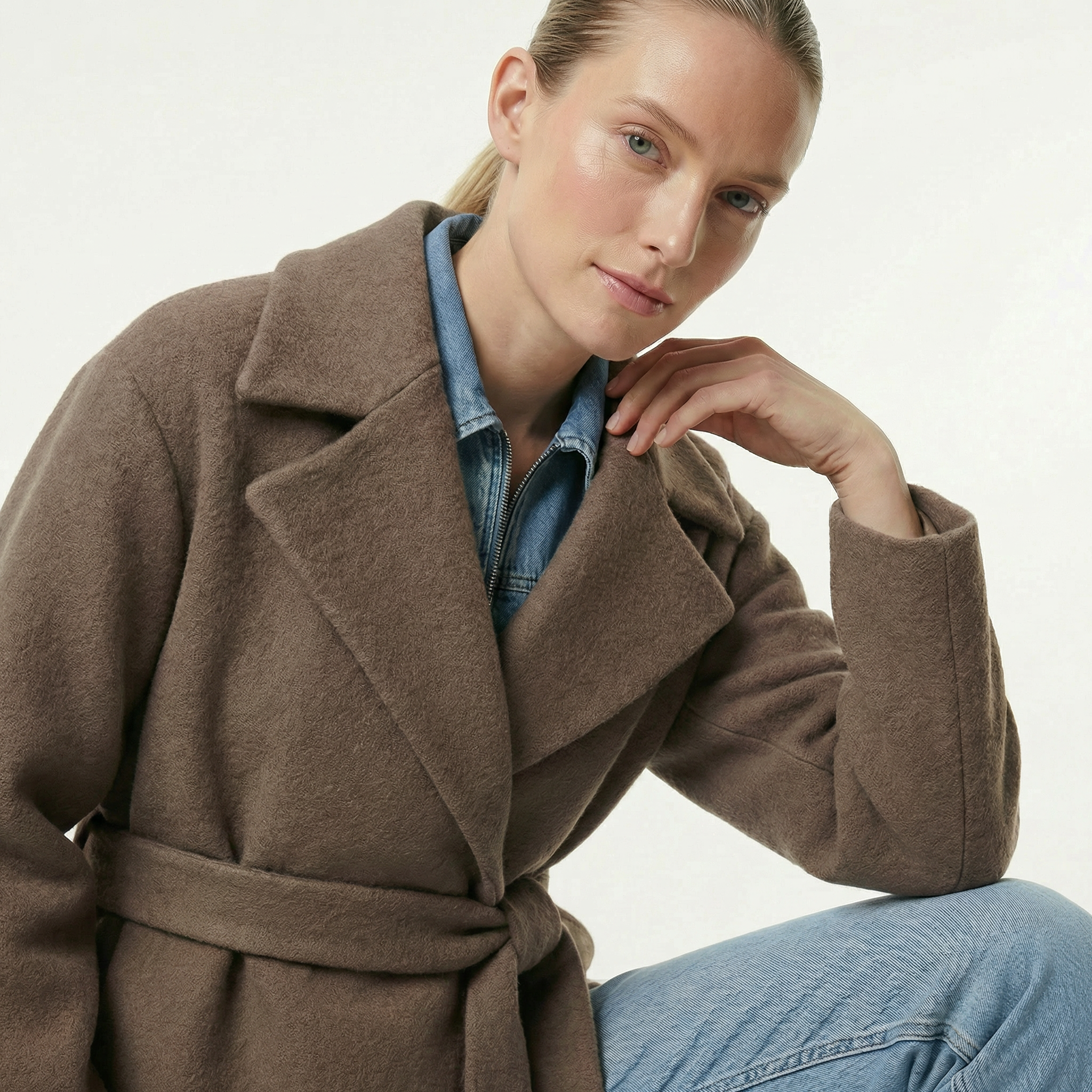 Woman wearing a brown coat over a denim shirt on a plain background